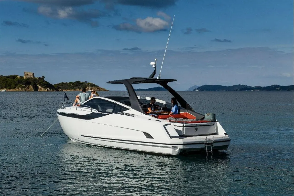 A sleek white boat with people on board, anchored in calm waters near an island with a castle in the background.